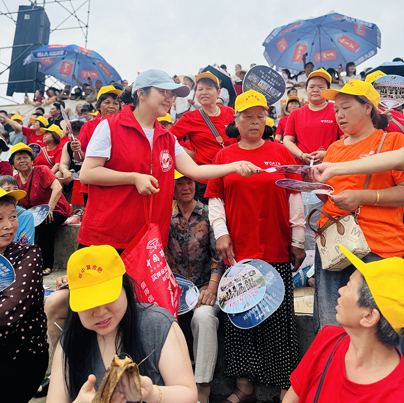 20250613816312.jpg 志愿者在大江口龙舟比赛现场为观赛者发放凉扇、粽子.jpg